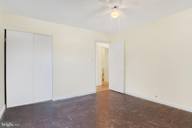 unfurnished bedroom featuring a ceiling fan, dark floors, baseboards, and a closet