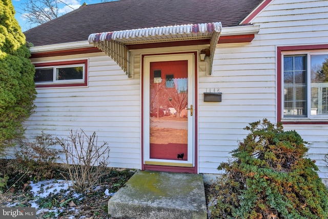 view of exterior entry featuring a shingled roof