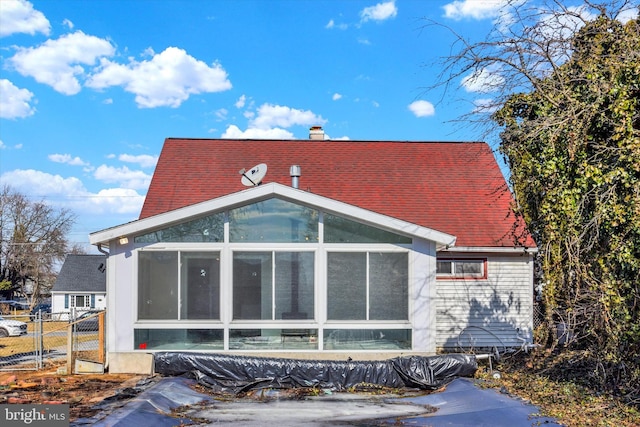 exterior space with a sunroom, a shingled roof, a chimney, and fence