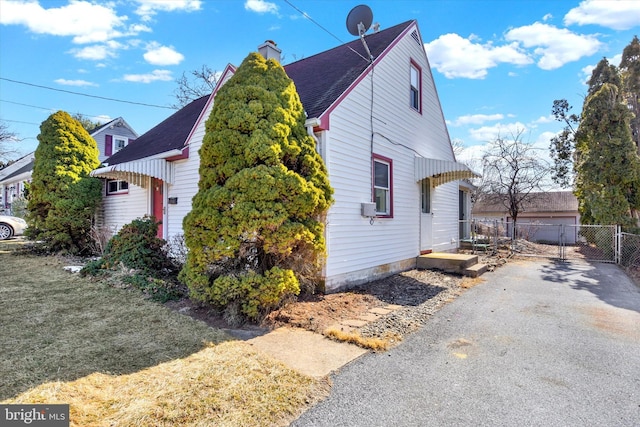 view of side of home with a chimney, fence, a lawn, and roof with shingles