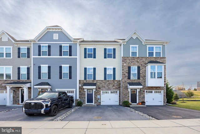 multi unit property featuring board and batten siding, stone siding, driveway, and a garage