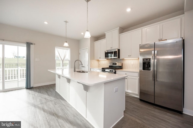 kitchen with light countertops, appliances with stainless steel finishes, white cabinetry, a sink, and an island with sink