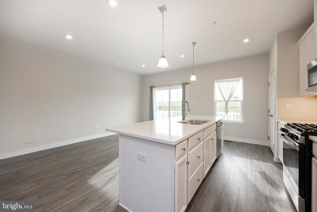 kitchen with a sink, light countertops, appliances with stainless steel finishes, a center island with sink, and pendant lighting