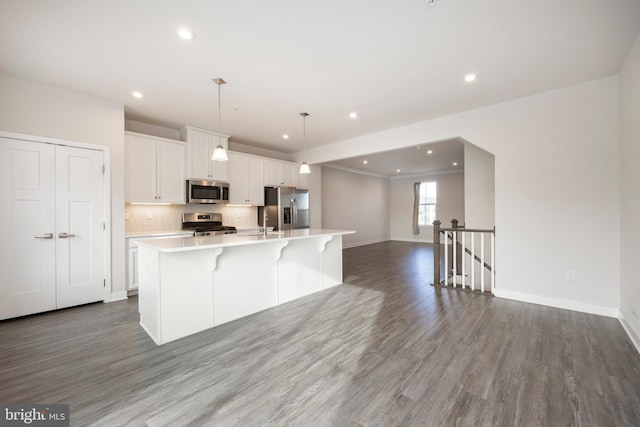 kitchen with stainless steel appliances, white cabinets, open floor plan, light countertops, and a large island with sink