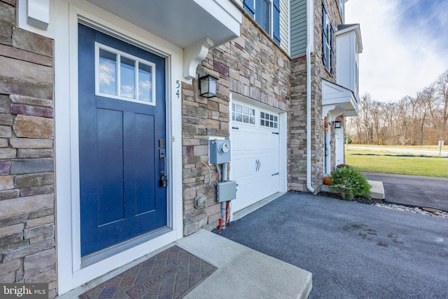 doorway to property with a garage, stone siding, and driveway