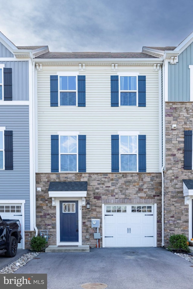 view of property featuring an attached garage, stone siding, and aphalt driveway