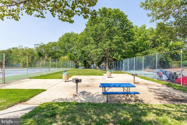 view of home's community featuring a tennis court, a lawn, and fence