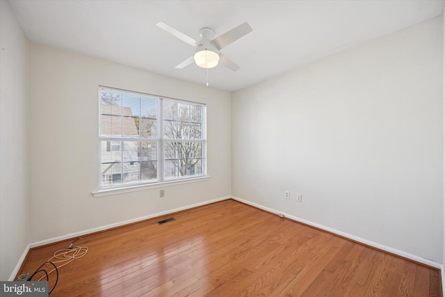 empty room featuring a ceiling fan, visible vents, baseboards, and wood finished floors