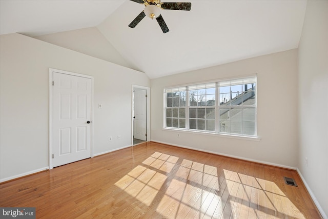 empty room featuring visible vents, ceiling fan, vaulted ceiling, wood finished floors, and baseboards