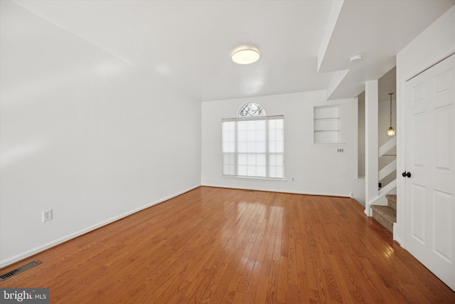 empty room featuring visible vents, stairway, baseboards, and hardwood / wood-style flooring