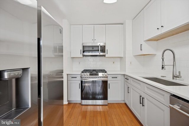 kitchen featuring light wood-style flooring, stainless steel appliances, a sink, white cabinetry, and light countertops