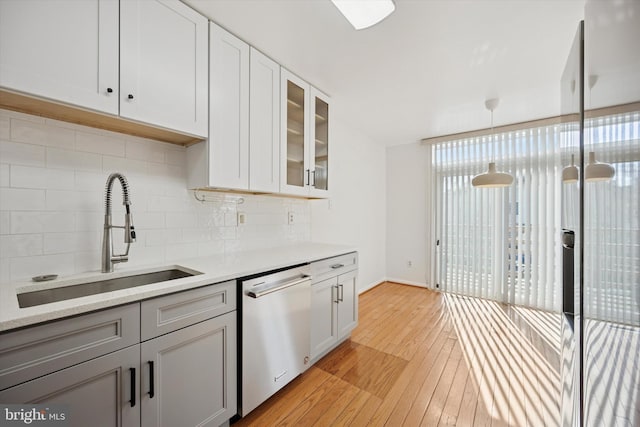 kitchen featuring decorative backsplash, glass insert cabinets, a sink, light wood-type flooring, and dishwasher