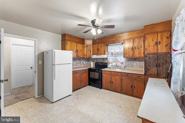 kitchen featuring under cabinet range hood, black electric range, light countertops, freestanding refrigerator, and brown cabinets