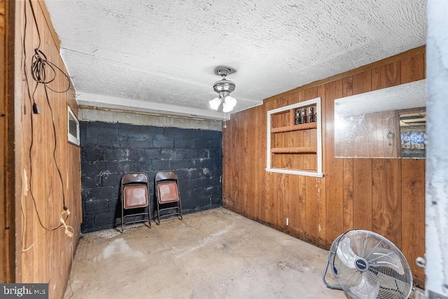 interior space featuring a textured ceiling, concrete floors, concrete block wall, and wooden walls