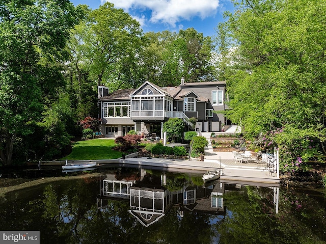 back of property with a water view, a sunroom, a yard, stairway, and a chimney