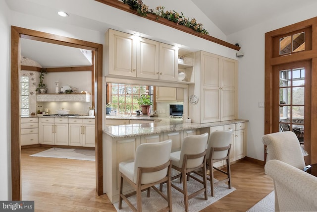 kitchen with lofted ceiling, light stone counters, cream cabinetry, a kitchen bar, and open shelves