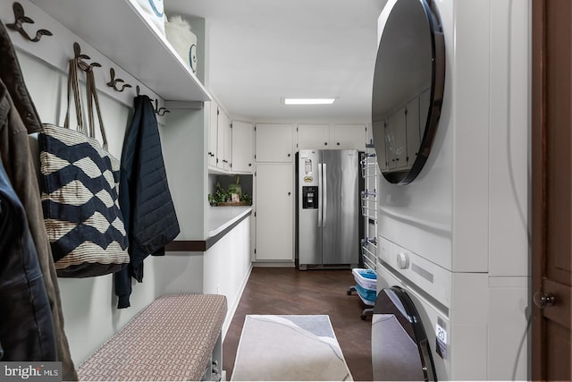 interior space with white cabinets, finished concrete flooring, light countertops, stacked washing maching and dryer, and stainless steel fridge with ice dispenser