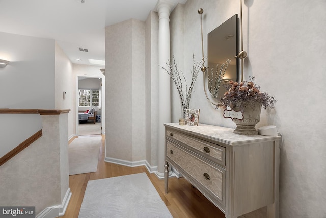 hallway featuring light wood-style flooring, visible vents, baseboards, and an upstairs landing