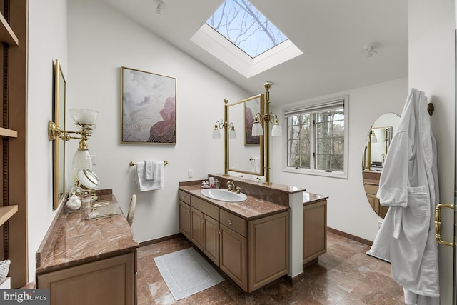 bathroom with vaulted ceiling with skylight, vanity, and baseboards