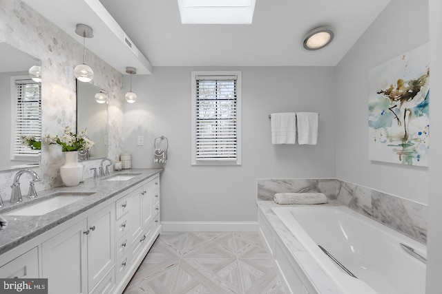 bathroom with a skylight, a garden tub, double vanity, a sink, and baseboards