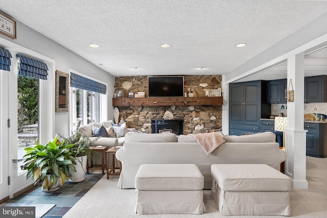 living area with stone tile flooring, recessed lighting, a textured ceiling, and a stone fireplace