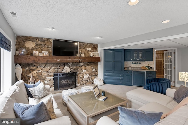 carpeted living room with indoor wet bar, visible vents, a stone fireplace, and a textured ceiling