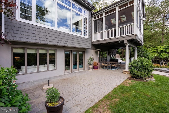 rear view of property featuring a patio, a sunroom, and stucco siding