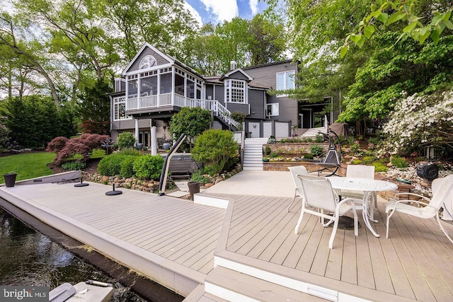 exterior space featuring a sunroom, stairway, outdoor dining area, and a deck with water view