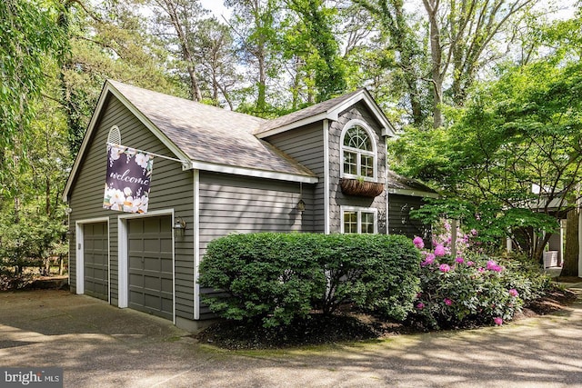 exterior space featuring a garage, roof with shingles, and driveway