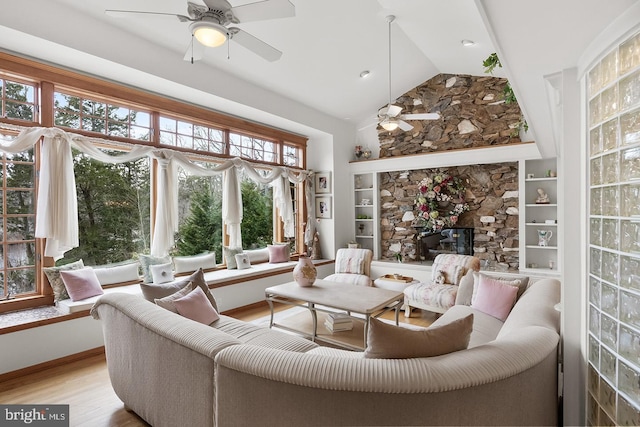 sunroom / solarium featuring a ceiling fan, vaulted ceiling, and a stone fireplace