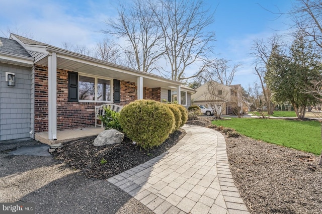 view of front of house with covered porch, brick siding, and a front lawn