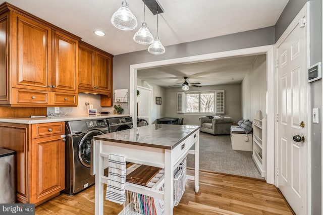 kitchen with brown cabinetry, light wood-style floors, open floor plan, ceiling fan, and washer and dryer