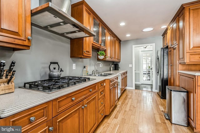 kitchen with wall chimney exhaust hood, brown cabinets, light countertops, stainless steel gas cooktop, and a sink