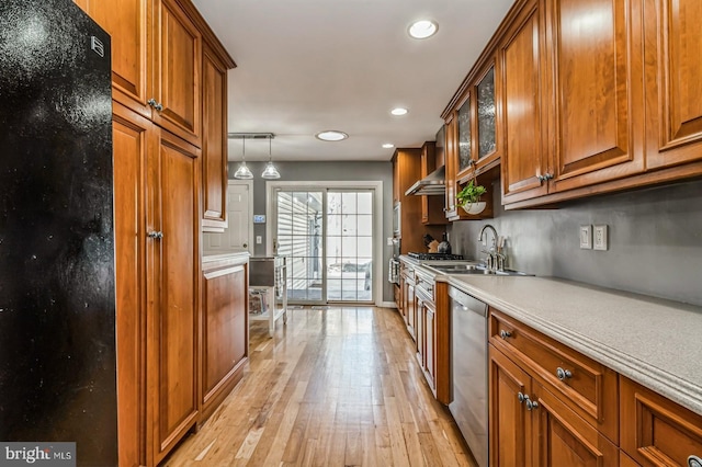 kitchen with a sink, freestanding refrigerator, dishwasher, light wood finished floors, and brown cabinetry