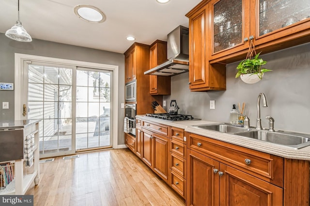 kitchen featuring stainless steel appliances, brown cabinetry, a sink, and wall chimney range hood