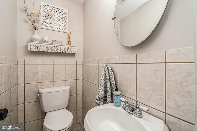 bathroom with a sink, tile walls, and toilet