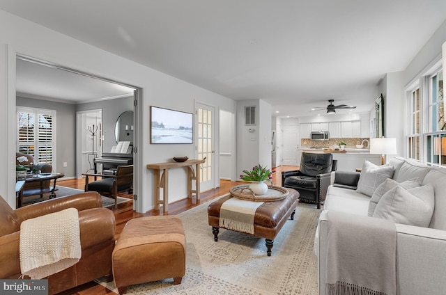 living area with light wood-type flooring, baseboards, visible vents, and ceiling fan