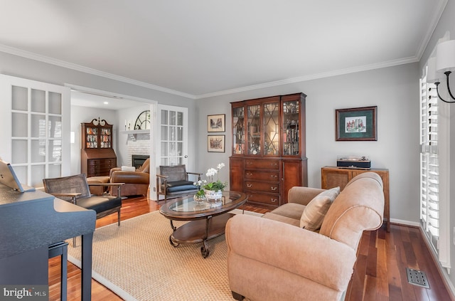 living area with crown molding, visible vents, a stone fireplace, wood finished floors, and baseboards