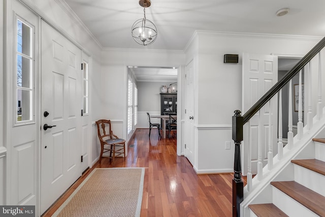 foyer featuring a notable chandelier, stairway, hardwood / wood-style floors, ornamental molding, and baseboards