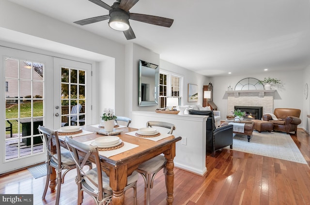 dining room with a brick fireplace, ceiling fan, french doors, and hardwood / wood-style flooring