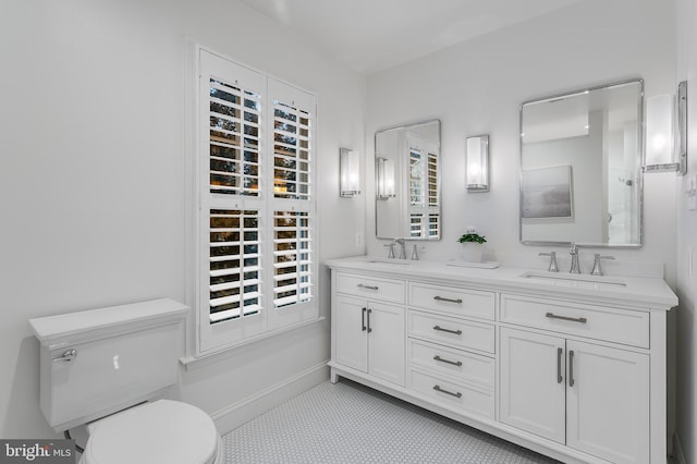 bathroom with double vanity, a sink, toilet, and baseboards