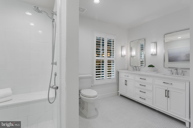 full bathroom featuring double vanity, visible vents, a tile shower, and a sink