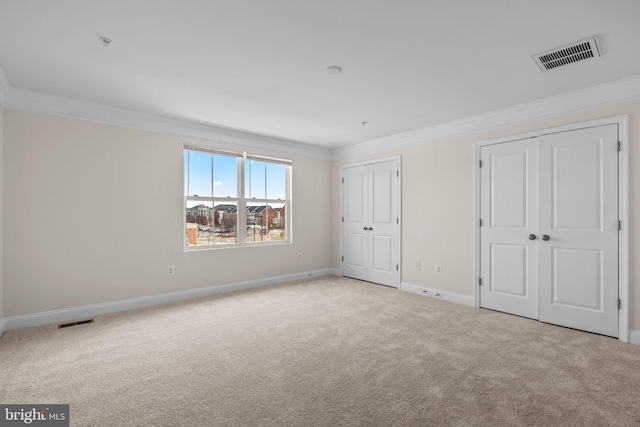 unfurnished bedroom with ornamental molding, two closets, visible vents, and light colored carpet