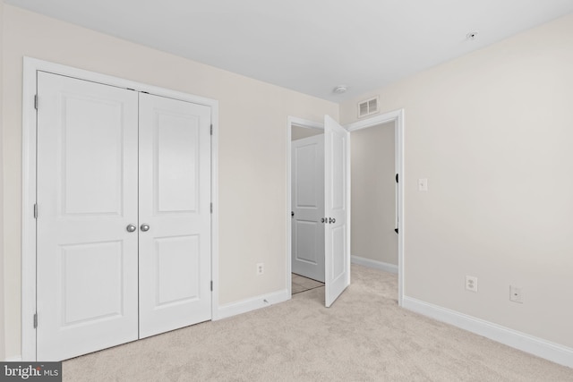 unfurnished bedroom with a closet, visible vents, light carpet, and baseboards