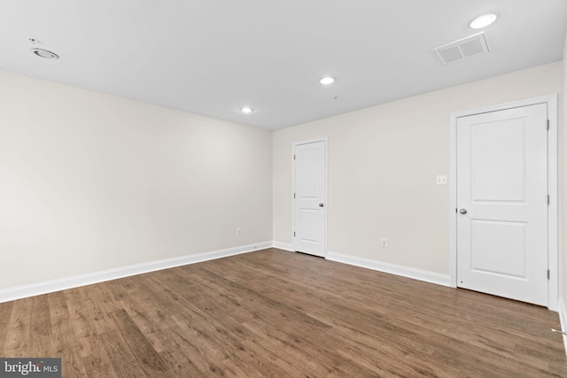 empty room with dark wood-style floors, visible vents, and baseboards