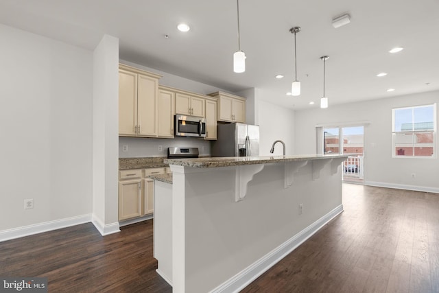 kitchen with stainless steel appliances, hanging light fixtures, an island with sink, and cream cabinets