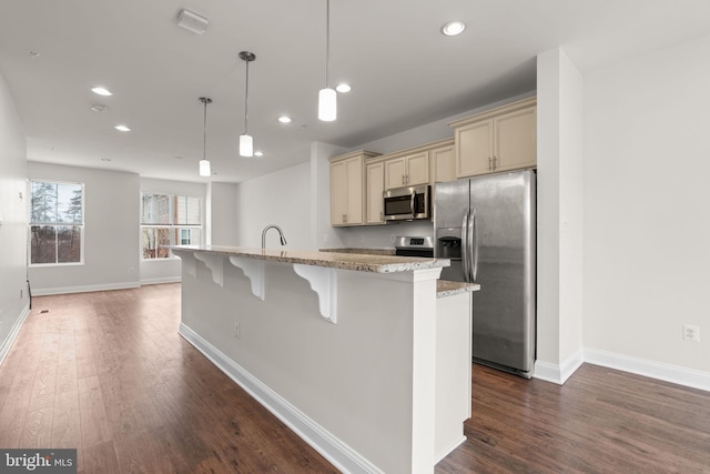 kitchen with stainless steel appliances, a kitchen island with sink, hanging light fixtures, and cream cabinets