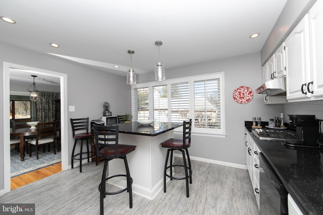 kitchen featuring under cabinet range hood, white cabinetry, light wood-style floors, dishwasher, and a kitchen bar