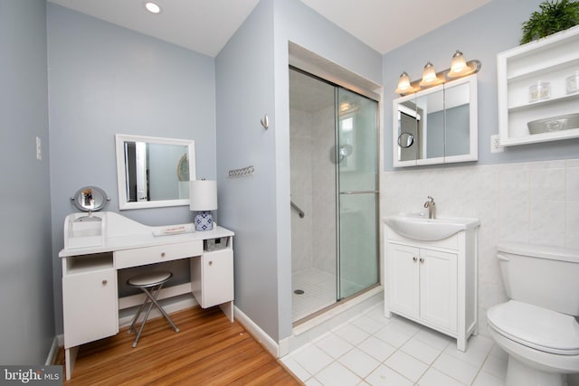 bathroom featuring a stall shower, toilet, wood finished floors, vanity, and tile walls