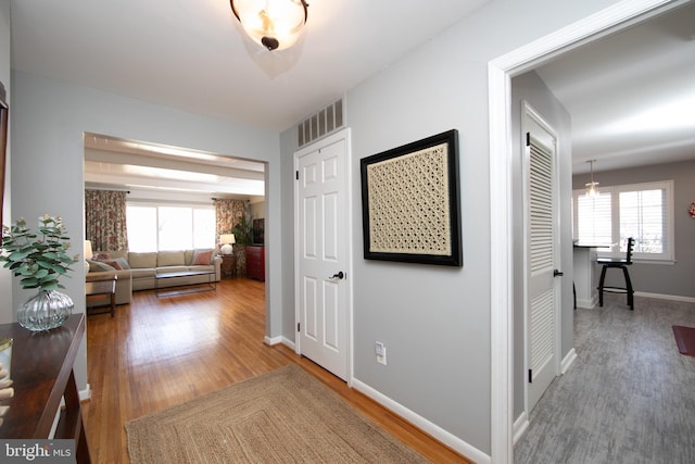 hallway featuring visible vents, baseboards, a wealth of natural light, and wood finished floors